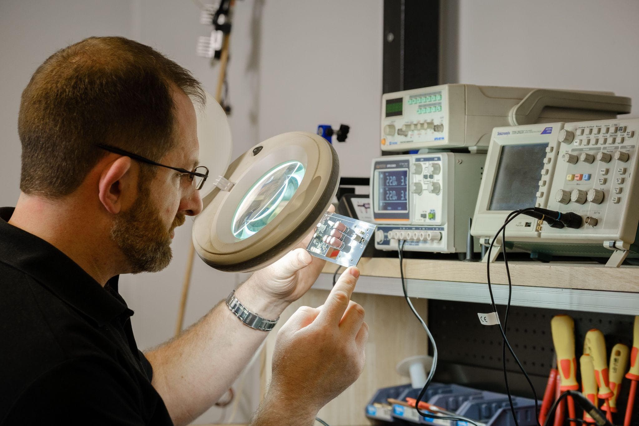 An engineer inspecting a circuit board under a bench magnifier